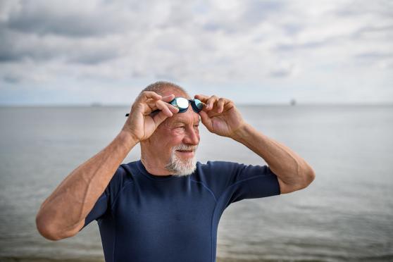A man holding his goggles on his forehead, a body of water in the background